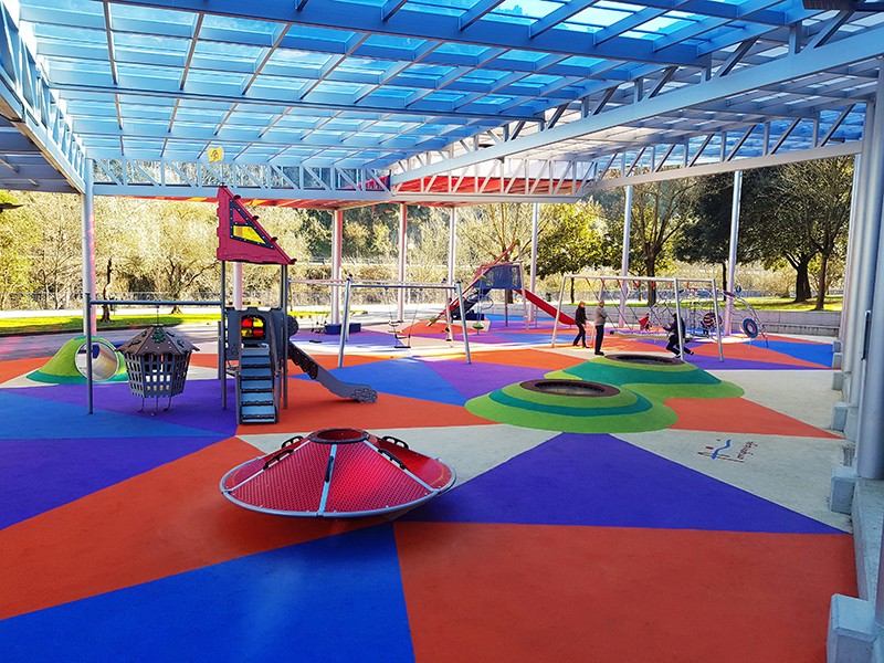 Parque infantil cubierto con suelo de colores y juegos inclusivos accesibles.