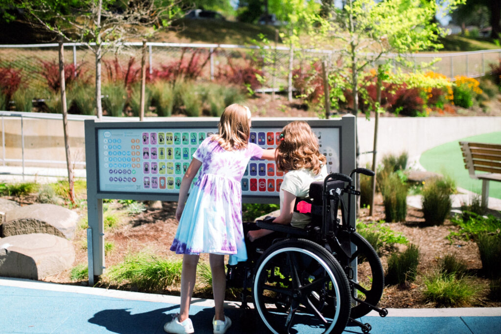 Servicios 10 Señalética inclusiva en un parque accesible, con panel informativo adaptado para niñas con y sin diversidad funcional.